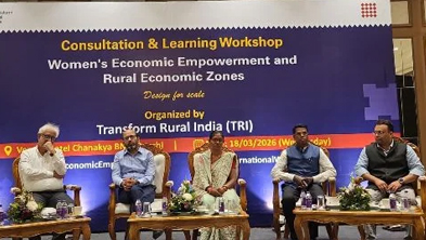Panel of six people seated on a stage in front of a banner for a workshop on women's economic empowerment and rural economic zones.