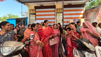 Group of Indian women in colorful sarees chatting near a temple doorway with orange-and-white striped walls in the background.