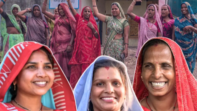 Group of smiling Indian women in bright sarees posing with arms raised outdoors.