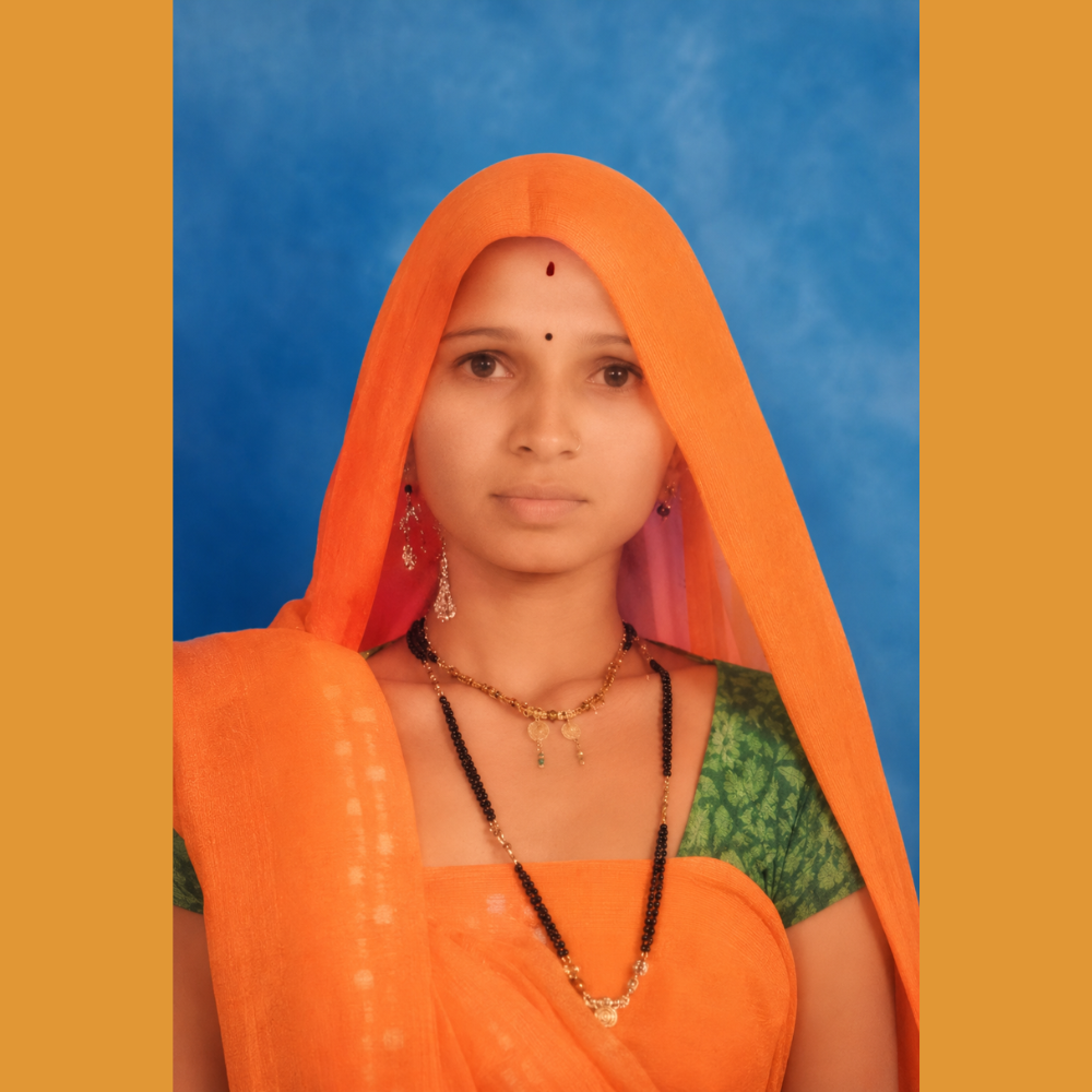 Portrait of a young woman in an orange saree with a green blouse, wearing earrings and necklaces, posed against a blue background.