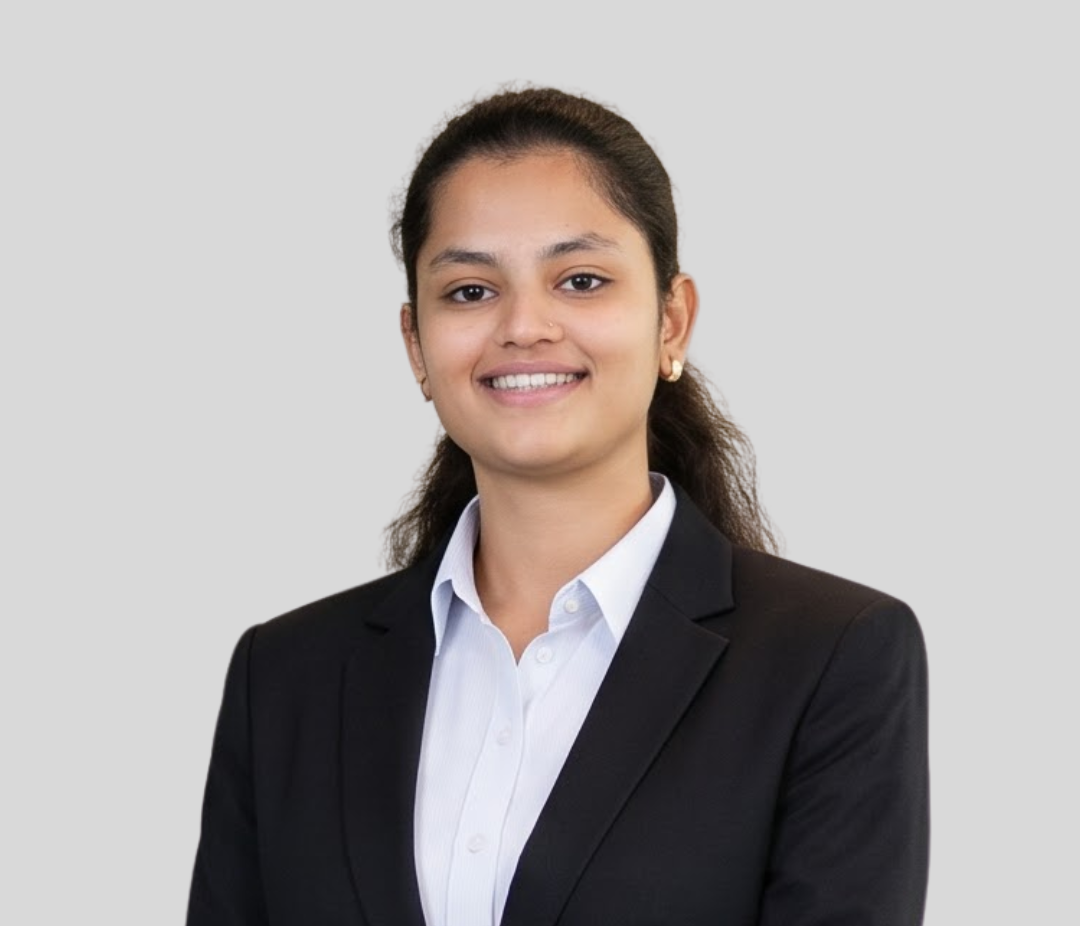 Professional headshot: woman in a black blazer and white shirt, smiling at the camera with a light gray background.