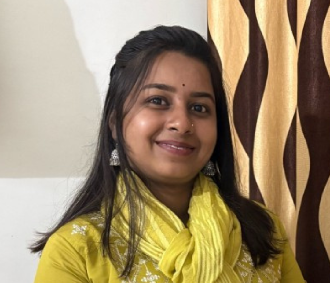 Smiling woman with long dark hair wearing a yellow scarf, silver earrings, and a small bindi visible on her forehead.